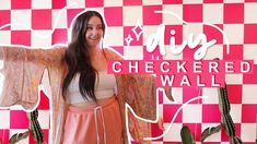 a woman standing in front of a checkered wall with her arms spread out to the side