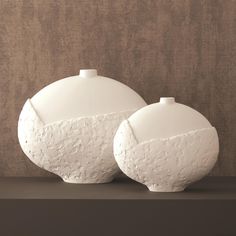 two white vases sitting side by side on a shelf in front of a wall