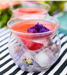 three clear bowls filled with different types of flowers and ice cubes on a striped tablecloth