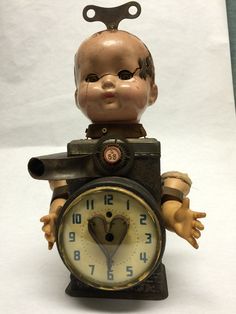 an old clock with a baby doll sitting on it's head and holding a wrench