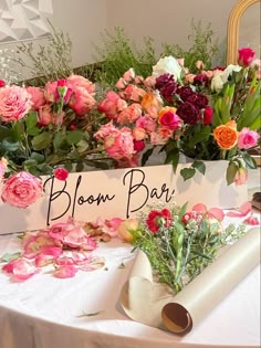 a table topped with flowers and a sign that says bloom bar next to some rolls of paper