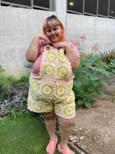 a woman in pink shirt and crochet shorts standing on grass with handbag