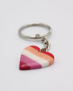 a striped heart shaped keychain on a white surface with a red, orange and pink stripe