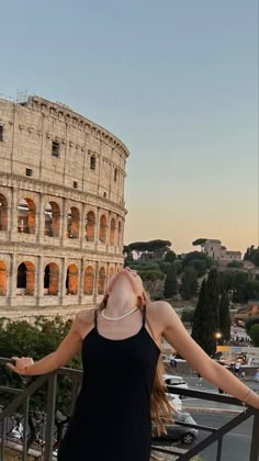 a woman standing on top of a balcony next to an old building and looking up at the sky