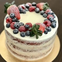 a cake with berries and blueberries on top is sitting on a wooden table, ready to be eaten