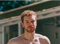 a shirtless man with no shirt standing in front of a building and looking at the camera