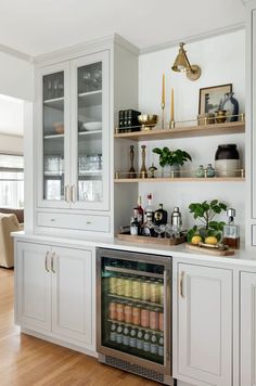 a kitchen with white cabinets and shelves filled with drinks on top of wooden flooring