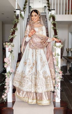 a woman in a white and gold wedding dress standing on stairs with flowers around her