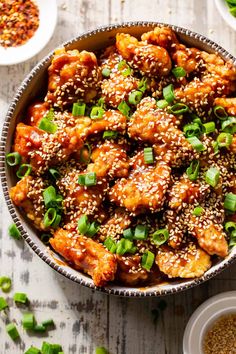 a bowl filled with sesame seed chicken and garnished with green onions on top