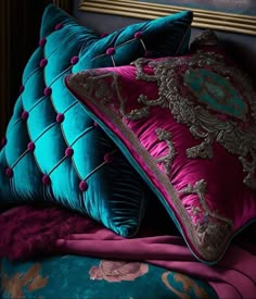 two blue and pink pillows sitting on top of a bed next to a framed painting