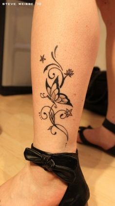 a woman's foot with a tattoo on it, and her black shoes are sitting on the floor