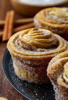 cinnamon rolls on a black plate covered in powdered sugar and topped with cinnamon sticks