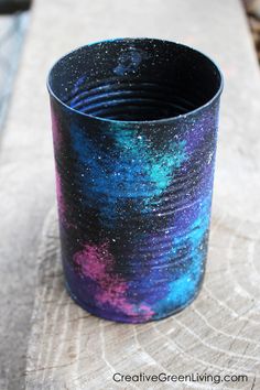 a cup that is sitting on top of a piece of wood with paint splattered on it