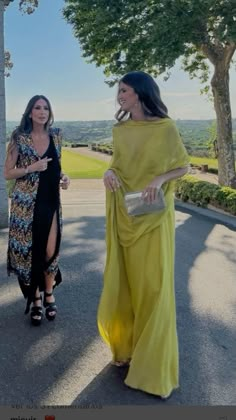 two women walking down the street in dresses and one is wearing a yellow shawl