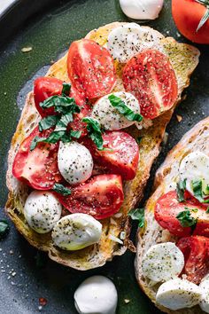 two pieces of bread with tomatoes, mozzarella and basil on them sitting on a black plate