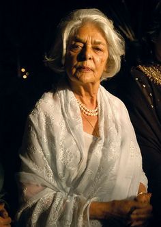 an older woman sitting next to another woman in a dark room with her hands on her hips