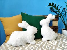 two white stuffed animals sitting on top of a bed next to pillows and planters