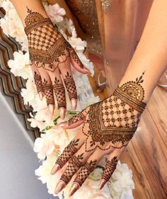 two hands with henna tattoos on them and white flowers in the background at a wedding