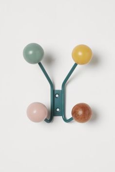 two balls are attached to a hook on a white wall, one is green and the other is yellow