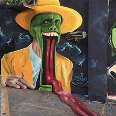 a painting on the side of a building with a person wearing a yellow hat and holding a long red object in his mouth