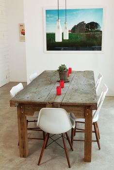 a wooden table with white chairs around it in front of a painting on the wall