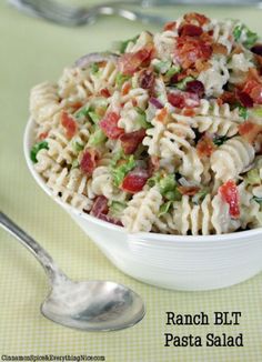 a pasta salad with bacon and other toppings in a white bowl on a green tablecloth