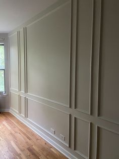 empty room with hard wood flooring and white paneling on the walls in front of a window