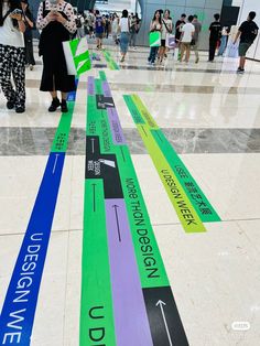 many people are walking through an airport with colorful signs on the floor and in front of them