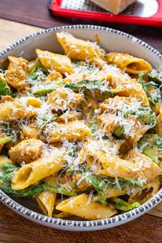 a bowl filled with pasta and vegetables covered in parmesan cheese on top of a wooden table