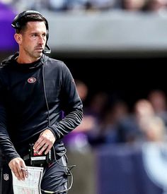 a man in black uniform holding a clipboard on top of his head while standing next to a football field