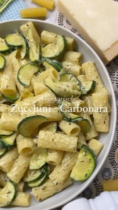 a white bowl filled with pasta and cucumbers next to some slices of cheese