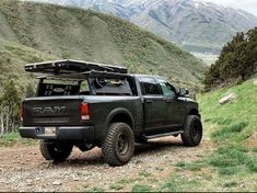 a black truck parked on the side of a dirt road with mountains in the background