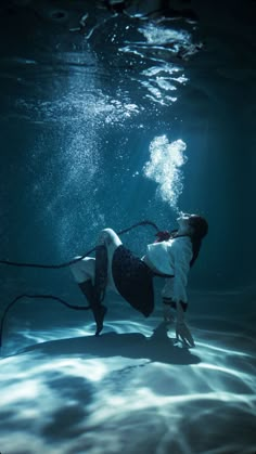 a woman in white shirt and black shorts holding a rope under water with light shining on her