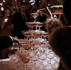 a table topped with lots of wine glasses filled with different types of drinks and people in the background