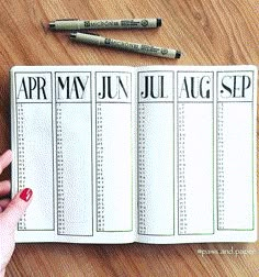 a person is holding an open planner with pencils next to it on a wooden table