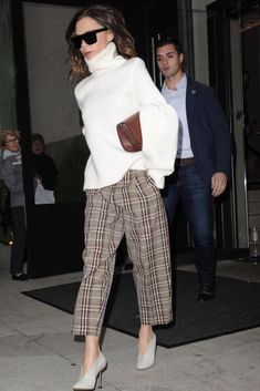 a woman in white sweater and plaid pants walking down the street with her hand on her hip