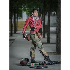 a man in red jacket and knee pads standing next to skateboard on the sidewalk