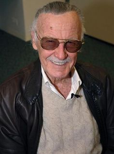 an older man wearing sunglasses and a leather jacket smiles at the camera while sitting down