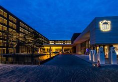 the building is lit up at night with lights on it's sides and reflecting in the water