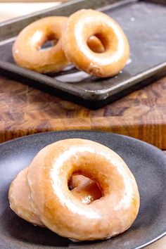 two glazed donuts sitting on top of a black plate