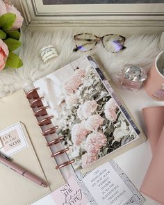 an open planner with pink flowers on it next to a cup of coffee and other items