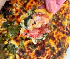 a hand holding up a piece of food over a white plate with green and red toppings