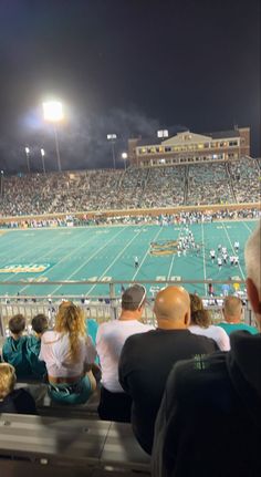 people sitting in the bleachers watching a football game at night with lights on