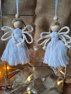 two white angel ornaments hanging from twine strings on a glass plate with lights in the background