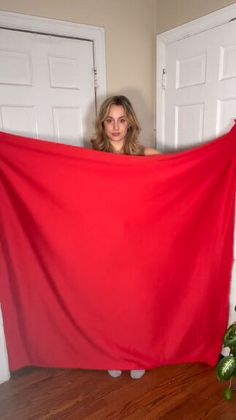 a woman holding up a red cloth in front of two white doors and a potted plant