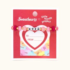 a pink bracelet with a heart and beads on the front, attached to a red card