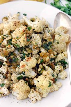 a white plate topped with cauliflower covered in seasoning next to lemon wedges