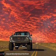 the truck is driving down the road with red clouds in the background