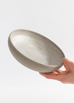 a hand holding a gray bowl in front of a white background with only one hand