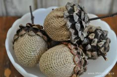 some pine cones are sitting in a white bowl on the table and one is covered with burlap